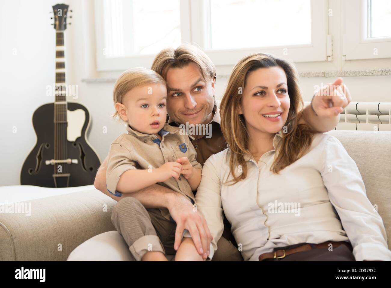 Portrait von glücklichen Eltern, die mit ihrem schönen Jungen auf dem Sofa sitzen. Zeigen mit dem Finger. Familienwerte. Stockfoto