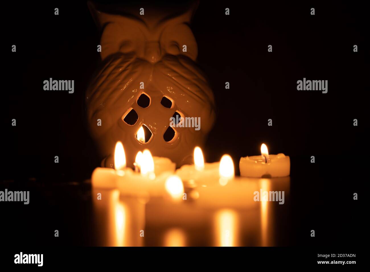 Eulenlaterne und Kerzen auf einem schwarzen Tisch mit dezenter Reflexion und schwarzem Hintergrund. Selektiver Fokus und negativer Raum Stockfoto