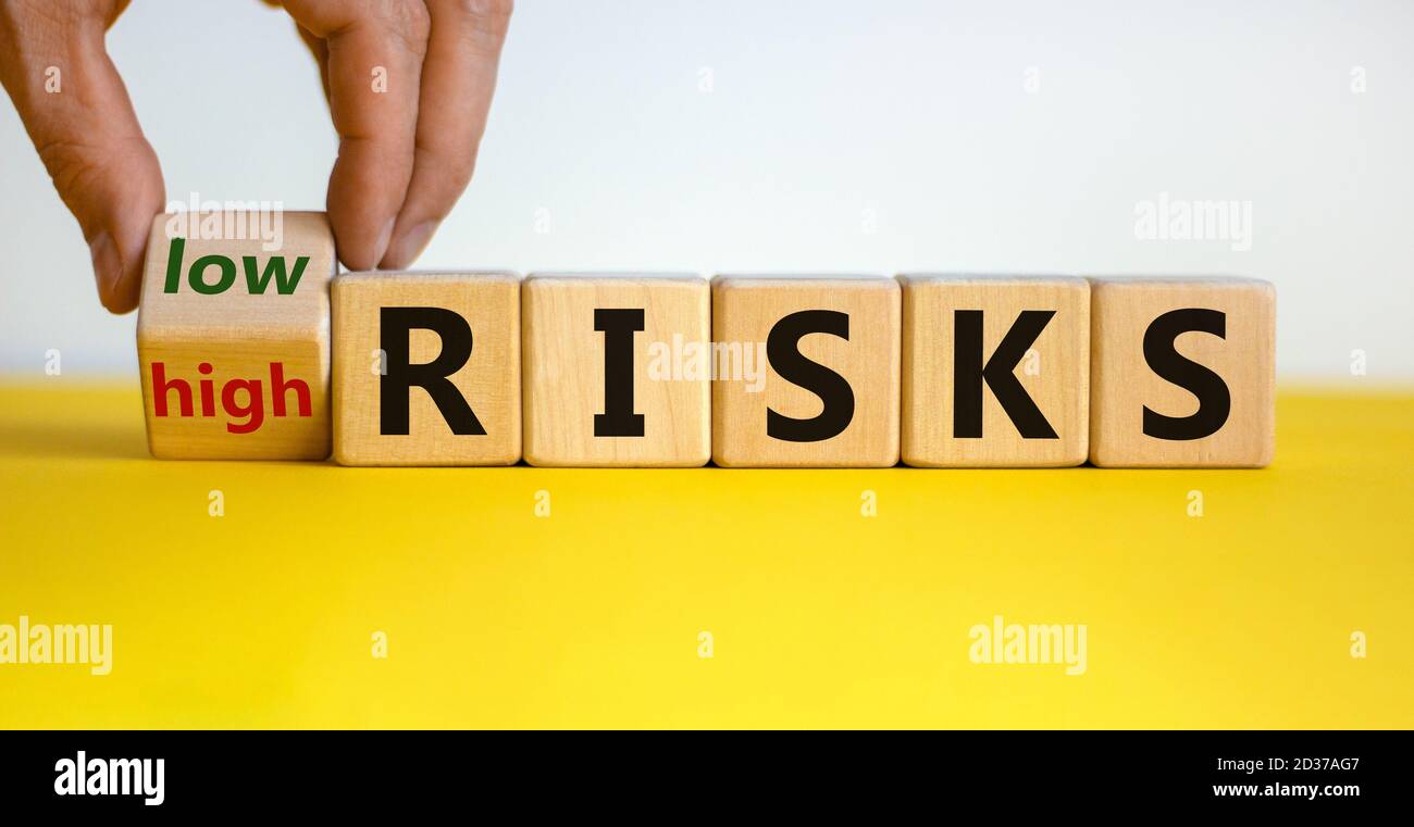Hand dreht einen Würfel und ändert die Worte "hohe Risiken" in "geringe Risiken" oder umgekehrt. Schöner gelber Tisch, weißer Hintergrund, Kopierraum. Unternehmen Stockfoto