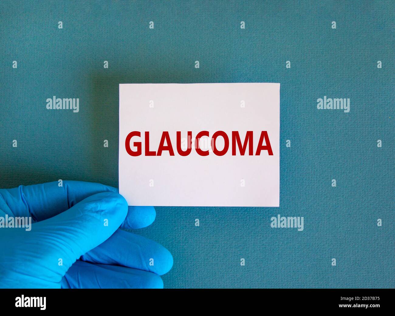 Hand in blauem Handschuh mit weißer Karte. Konzeptwort „Glaukom“. Medizinisches Konzept. Kopierbereich, schöner blauer Hintergrund. Stockfoto