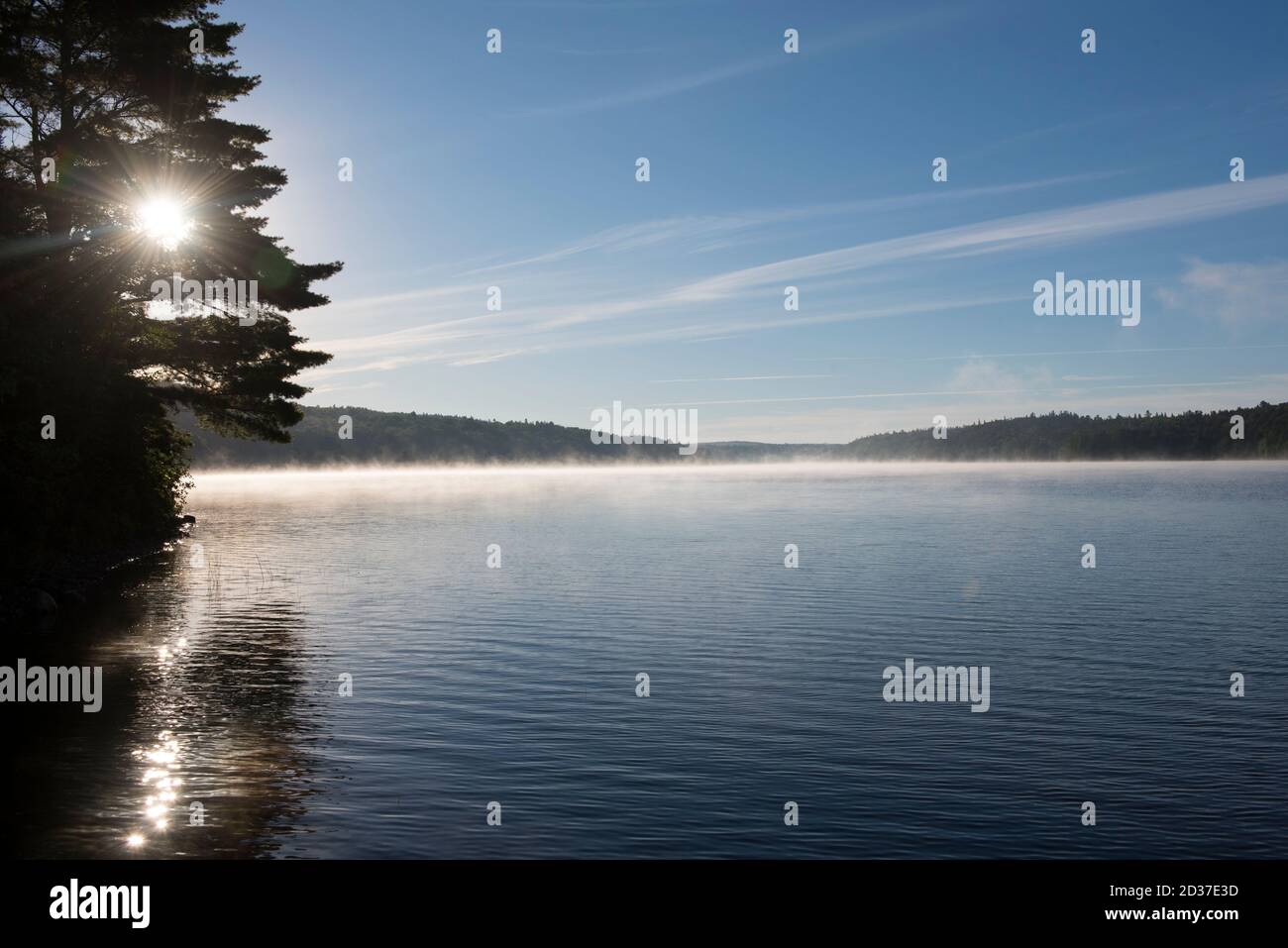 Sonnenaufgang auf einem See im Norden von Ontario. Blauer Himmel, ruhiges Wasser an einer Uferlinie mit Bäumen Stockfoto