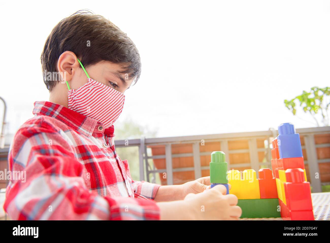 Nette Kinder Junge spielt in Terrasse Bausteine mit Gesichtsmaske Schutz. Selbstisolierung vom covid-19-Virus Stockfoto