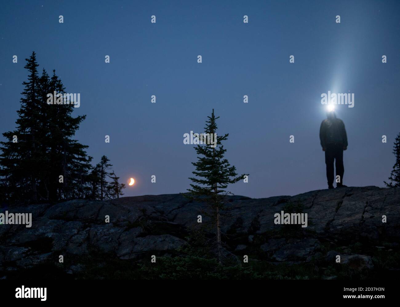 Mann steht auf dem Bergrücken, nachts mit aufgelaufter Stirnlampe. Stockfoto