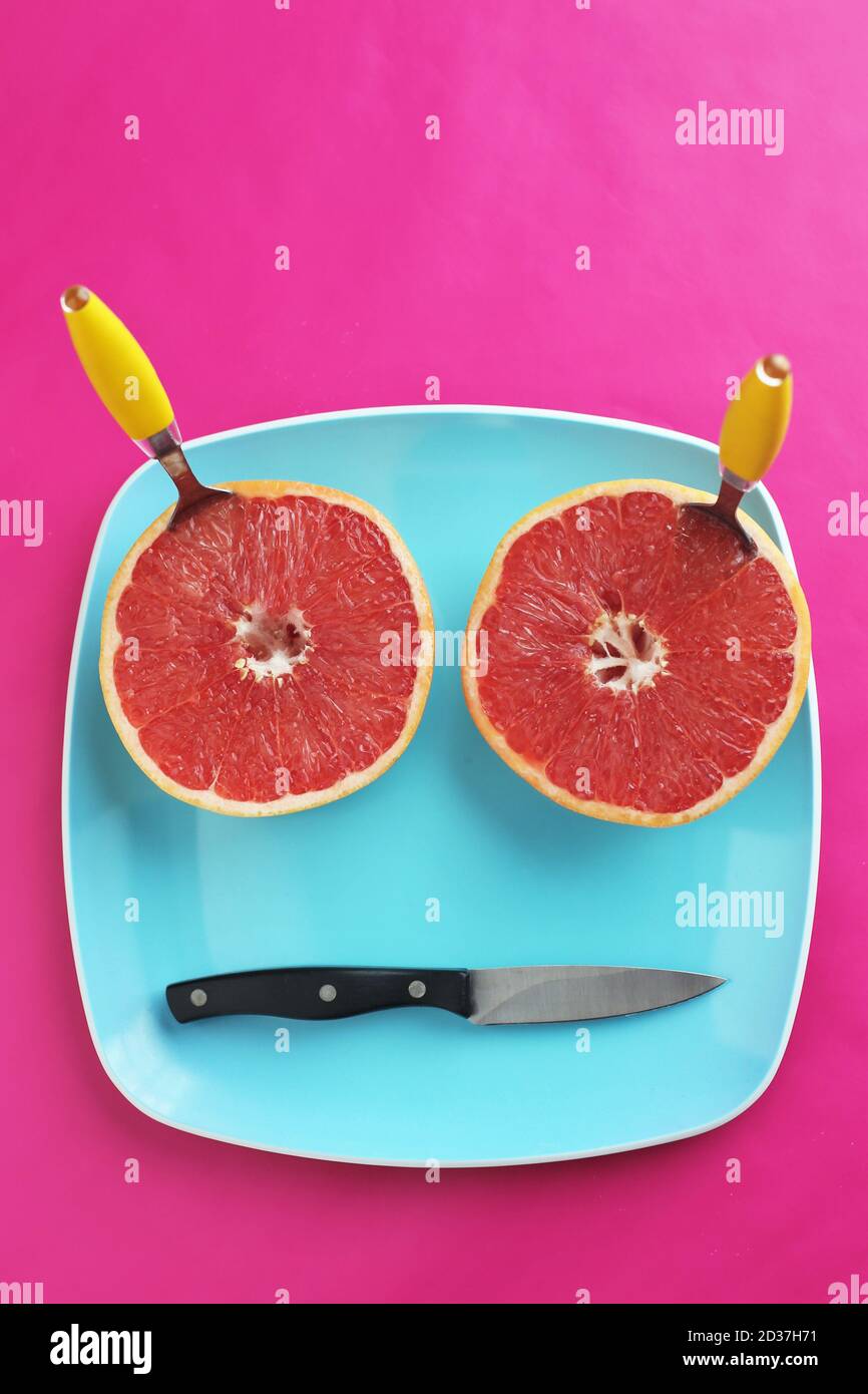 Eine Grapefruit in zwei Hälften geschnitten und angeordnet, um wie ein Gesicht auf einem Teller aussehen. Stockfoto