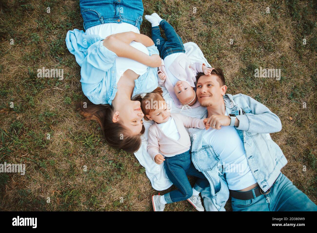 Foto von fröhlichen jungen Familie mit ihren Baby-Kinder im Freien auf Gras im Park, Familie Zeit. Stockfoto