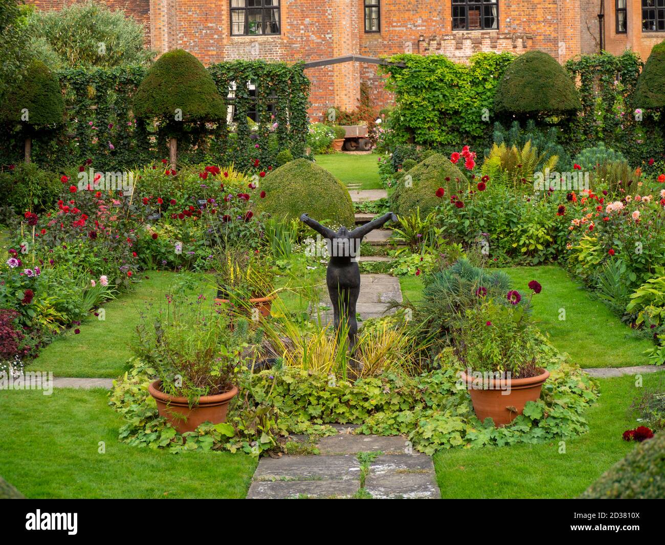 Chenies Manor House in Sun; der versunkene Garten im September mit Alan Biggs Skulptur von 'The Diver', die durch die lebendige Dahlia-Ausstellung reicht. Stockfoto