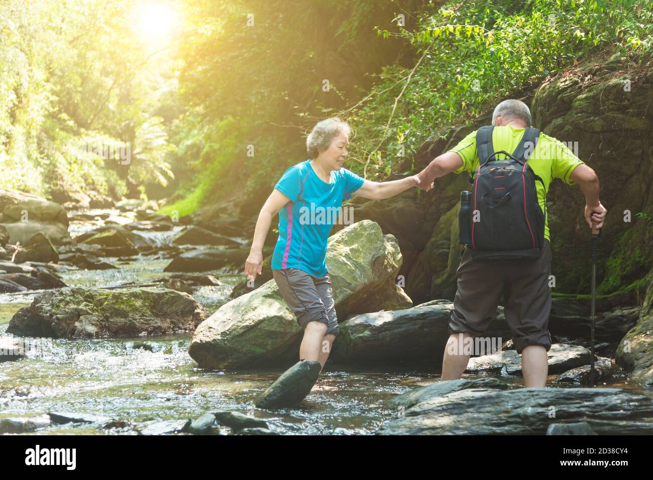 Asiatisches Seniorenpaar, das im Naturpark über einen kleinen Fluss läuft Stockfoto