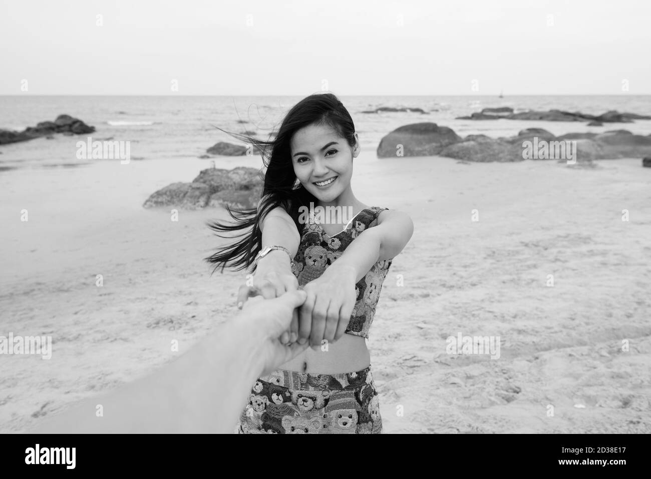 Junge glücklich schöne asiatische Frau lächelnd, während halten mit beiden Hände und führender Mann am Strand Stockfoto