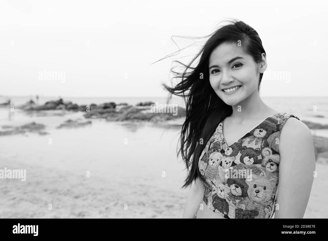 Junge glücklich schöne asiatische Frau an der windigen öffentlichen Strand von Hua Hin in Thailand lächelnd Stockfoto