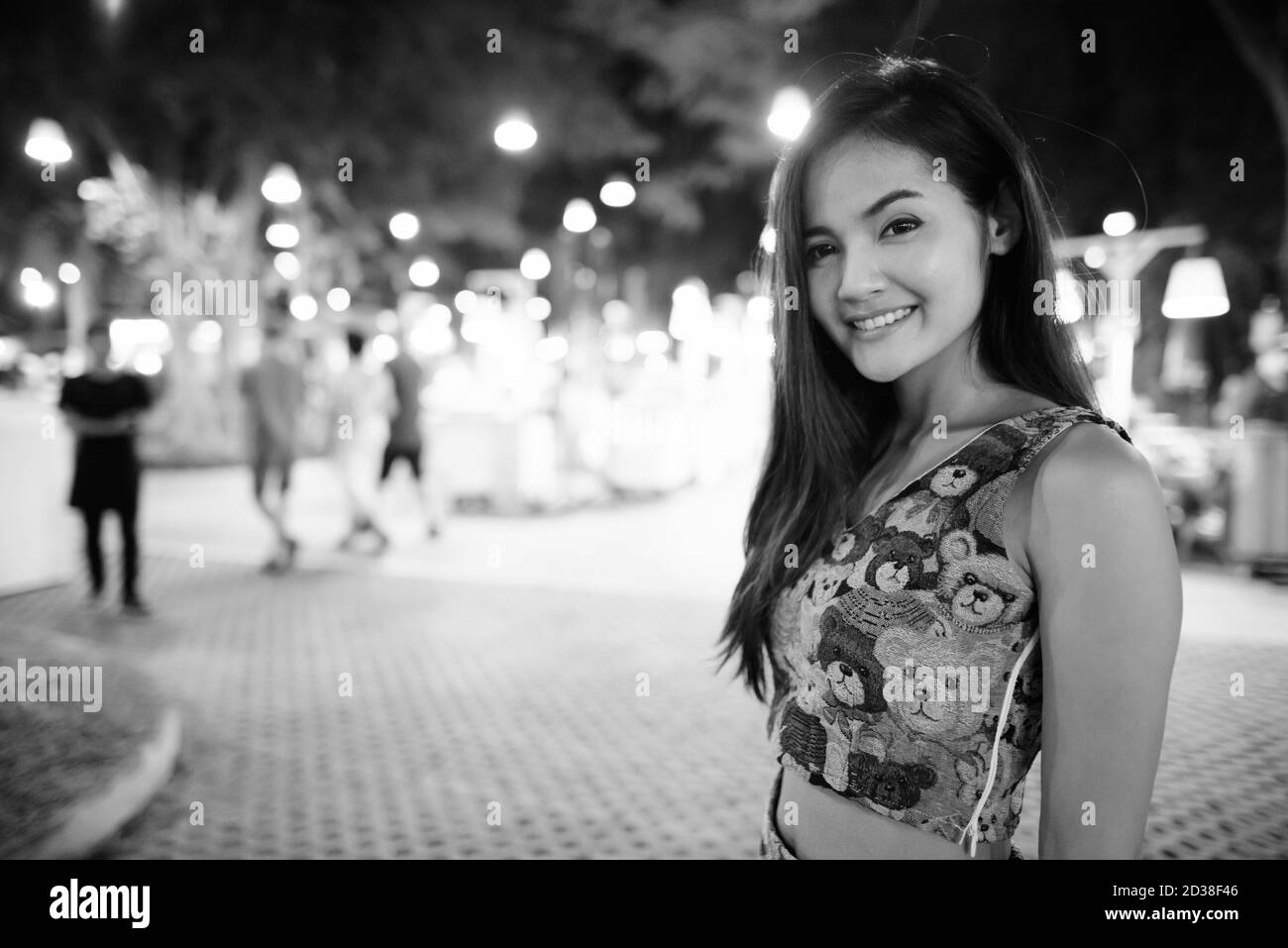 Junge asiatische Frau glücklich gegen die malerische Aussicht auf den Nachtmarkt in Hua Hin Thailand lächelnd Stockfoto