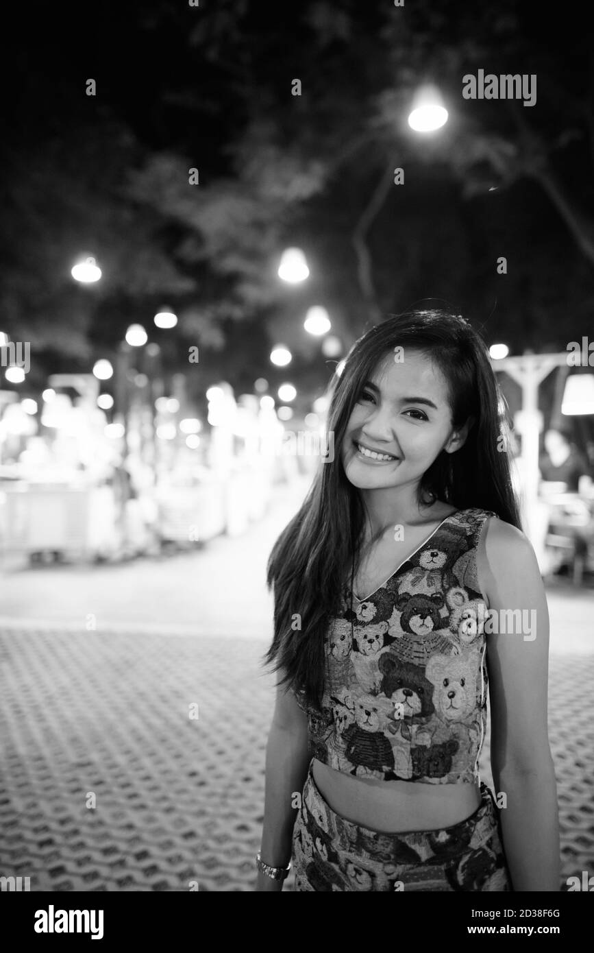 Junge glücklich schöne asiatische Frau lächelnd gegen die malerische Aussicht auf den Nachtmarkt in Hua Hin Thailand verkaufen verschiedene Lebensmittel Stockfoto