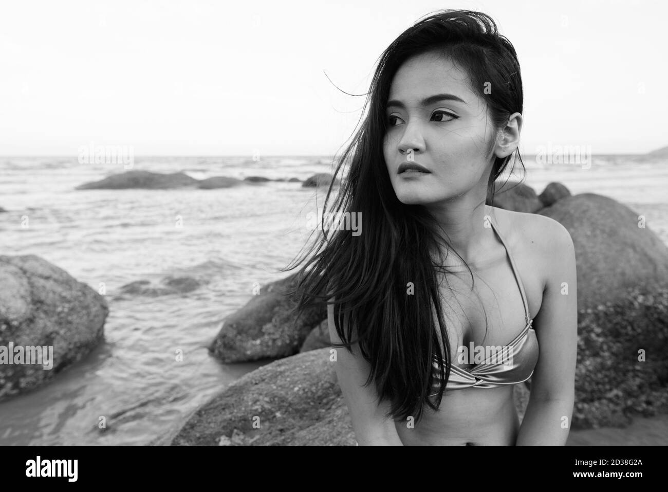 Junge schöne asiatische Frau denken und auf Entfernung, während an den Felsen der öffentliche Strand in Hua Hin Thailand sitzen Stockfoto