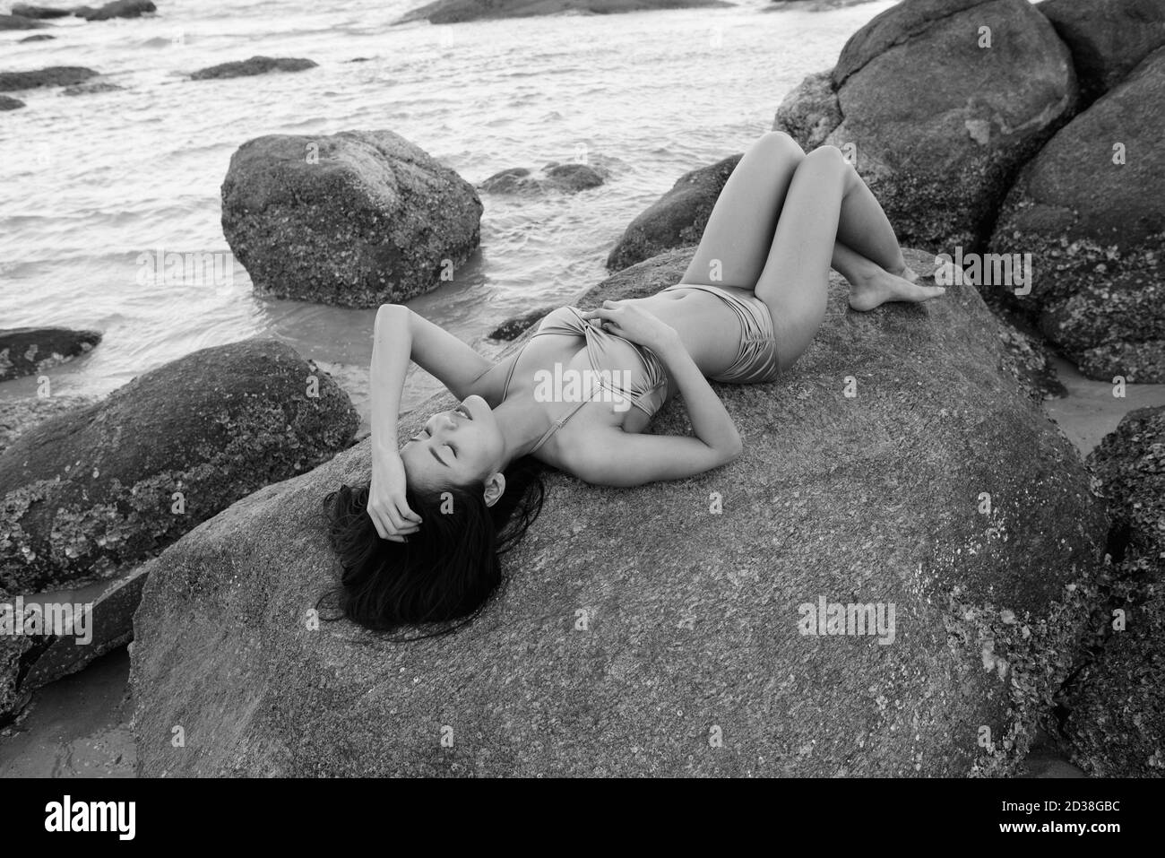 Junge schöne asiatische Frau liegend, während mit Blick auf die Felsen der öffentliche Strand in Hua Hin Thailand geschlossen. Stockfoto