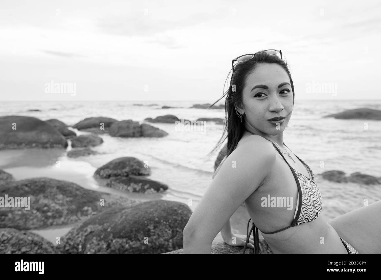 Junge schöne asiatische Frau denken beim Sitzen auf den Felsen der öffentliche Strand in Hua Hin Thailand Stockfoto