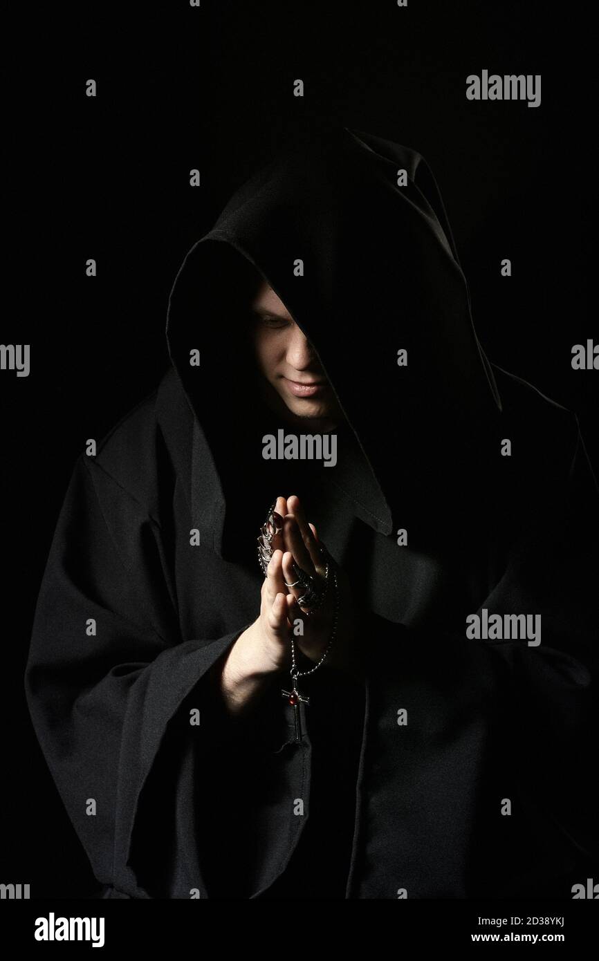 Assassin in dunkler Kleidung in der Kirche. Zauberer in schwarzem Mantel tun geheimnisvollen Ritus in dunklen Raum. Mönch betet in der Dunkelheit. Magisches Ritual im Schatten. Sinn Stockfoto