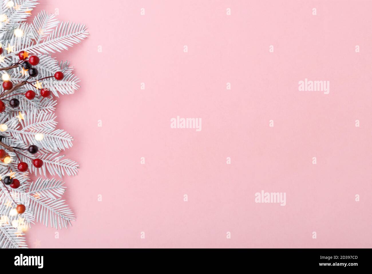 Weihnachtliche Umrandung mit Tannenzweigen, Eberesche und goldenen Lichtern auf pastellrosa Hintergrund Stockfoto