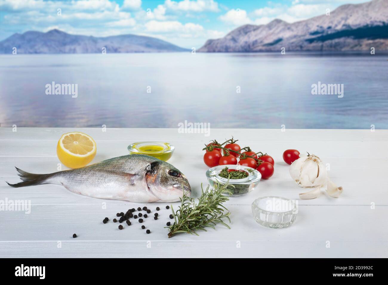 Eine Seebrasse und mit Produkten für die Herstellung von Ein Rezept auf einem weißen Holztisch mit dem Meer bucht im Hintergrund Stockfoto