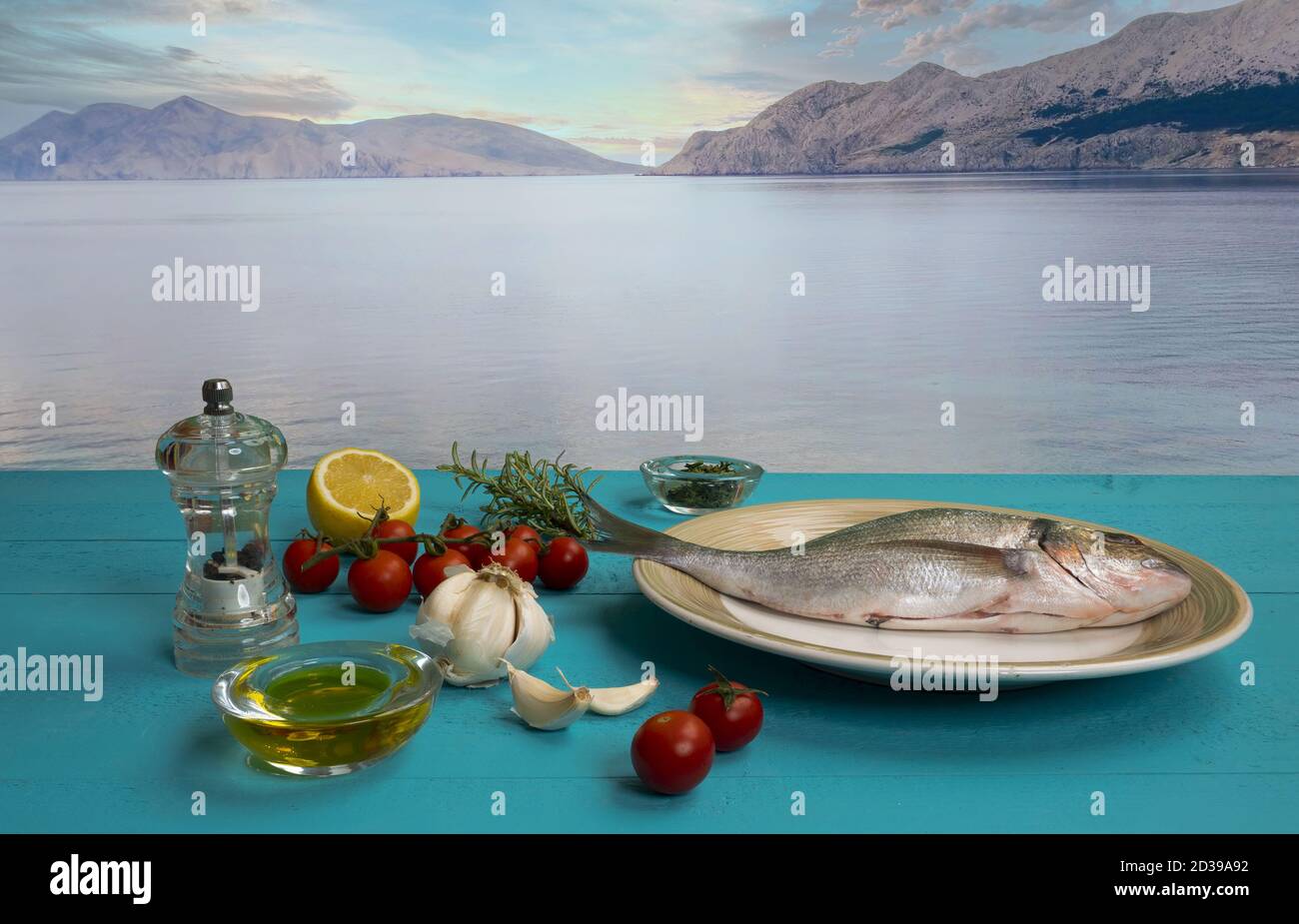 Eine Seebrasse und mit Produkten für die Herstellung von Ein Rezept auf einem blauen Holztisch mit dem Meer bucht im Hintergrund Stockfoto