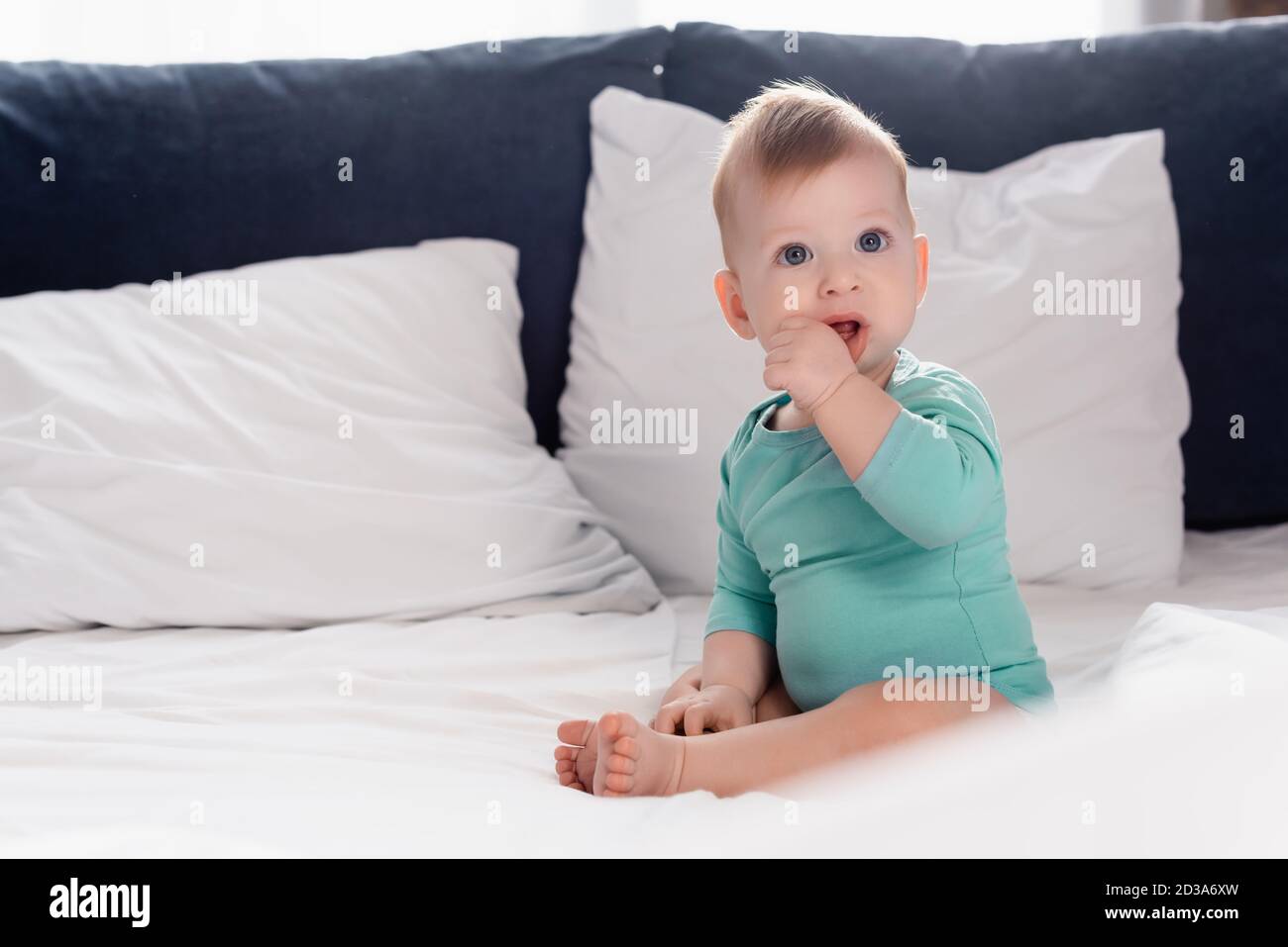 Selektiver Fokus des Kleinkindes im Babytromper sitzend Bett mit Hand im Mund Stockfoto