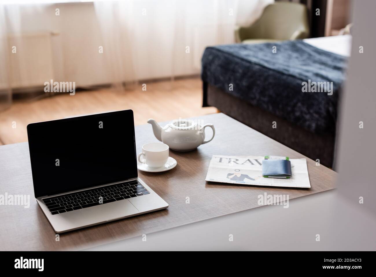 Laptop mit leerem Bildschirm in der Nähe von Teekanne, Tasse, Reisezeitung und Reisepass mit Flugticket auf dem Tisch Stockfoto