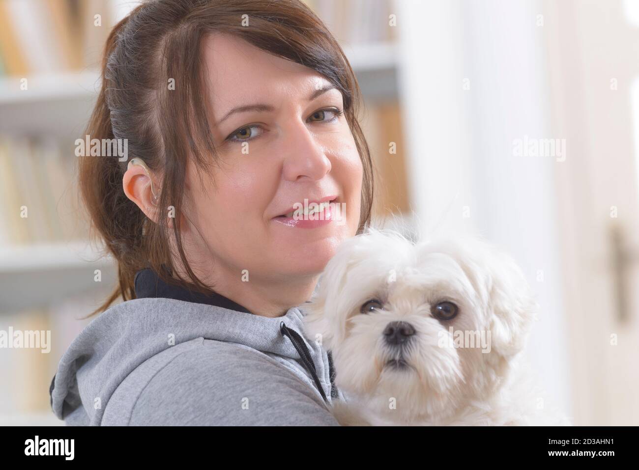 Junge, lächelnde Frau tragen Deaf Aid und ihrem kleinen Hund Holding Stockfoto