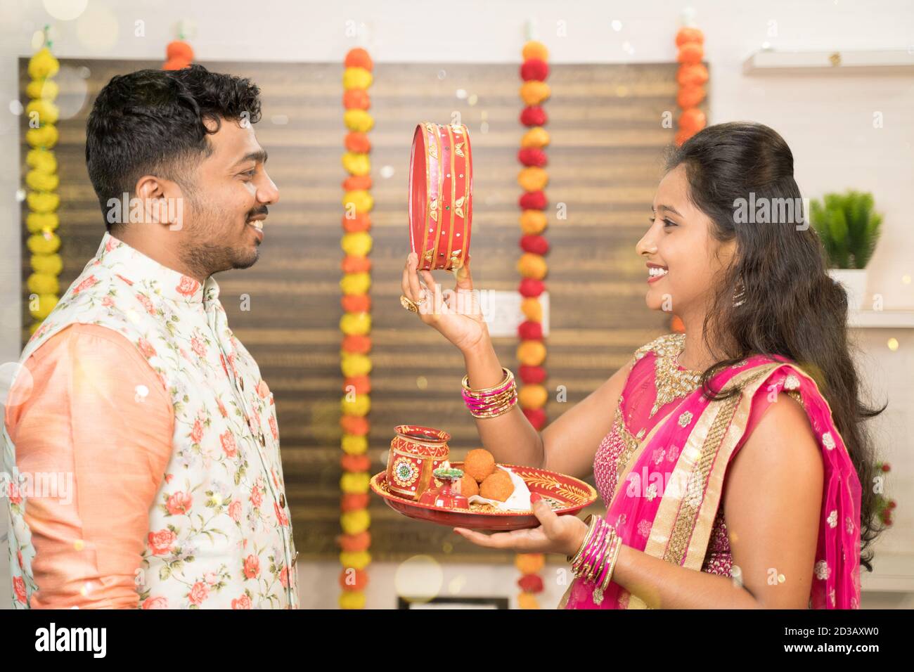 Indische Frau in traditioneller Kleidung sieht ihren Mann oder Partner durch Sieb während der Hindu indischen religiösen karwa Chauth Festival zu Hause. Stockfoto