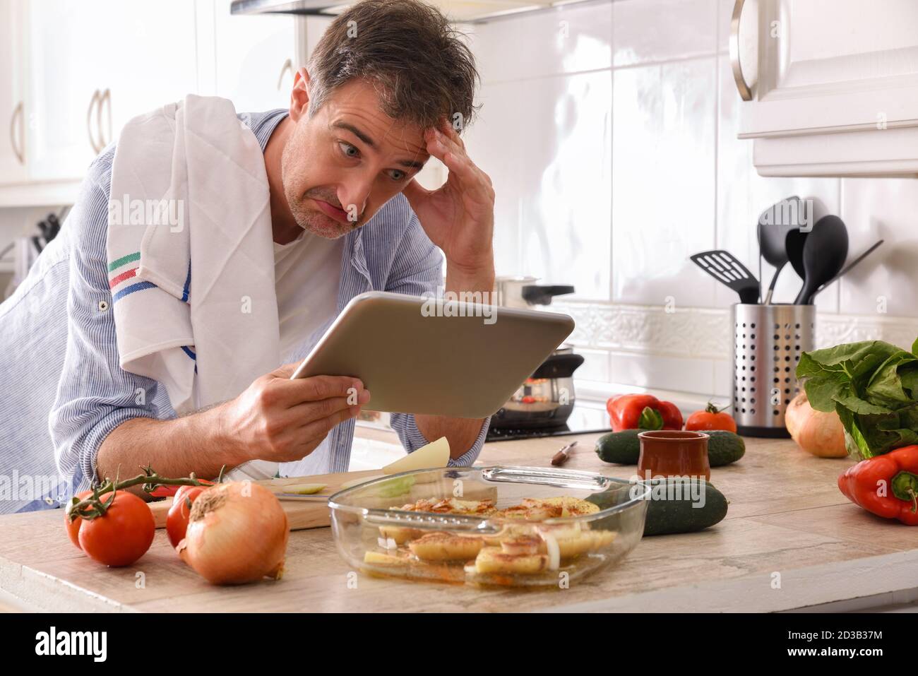 Anfänger Koch Blick auf eine Tablette mit einem unfähigen Gesicht Seinen Ellbogen auf der Küchenbank auflegen und seine Stirn berühren Stockfoto