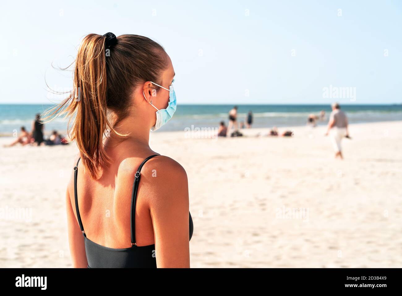 Strand und die Maske. Frau trägt Gesichtsmask während Corona-Virus Pandemie zum Schutz. Dame, die die Menschenmenge im Urlaub betrachtet. Stockfoto
