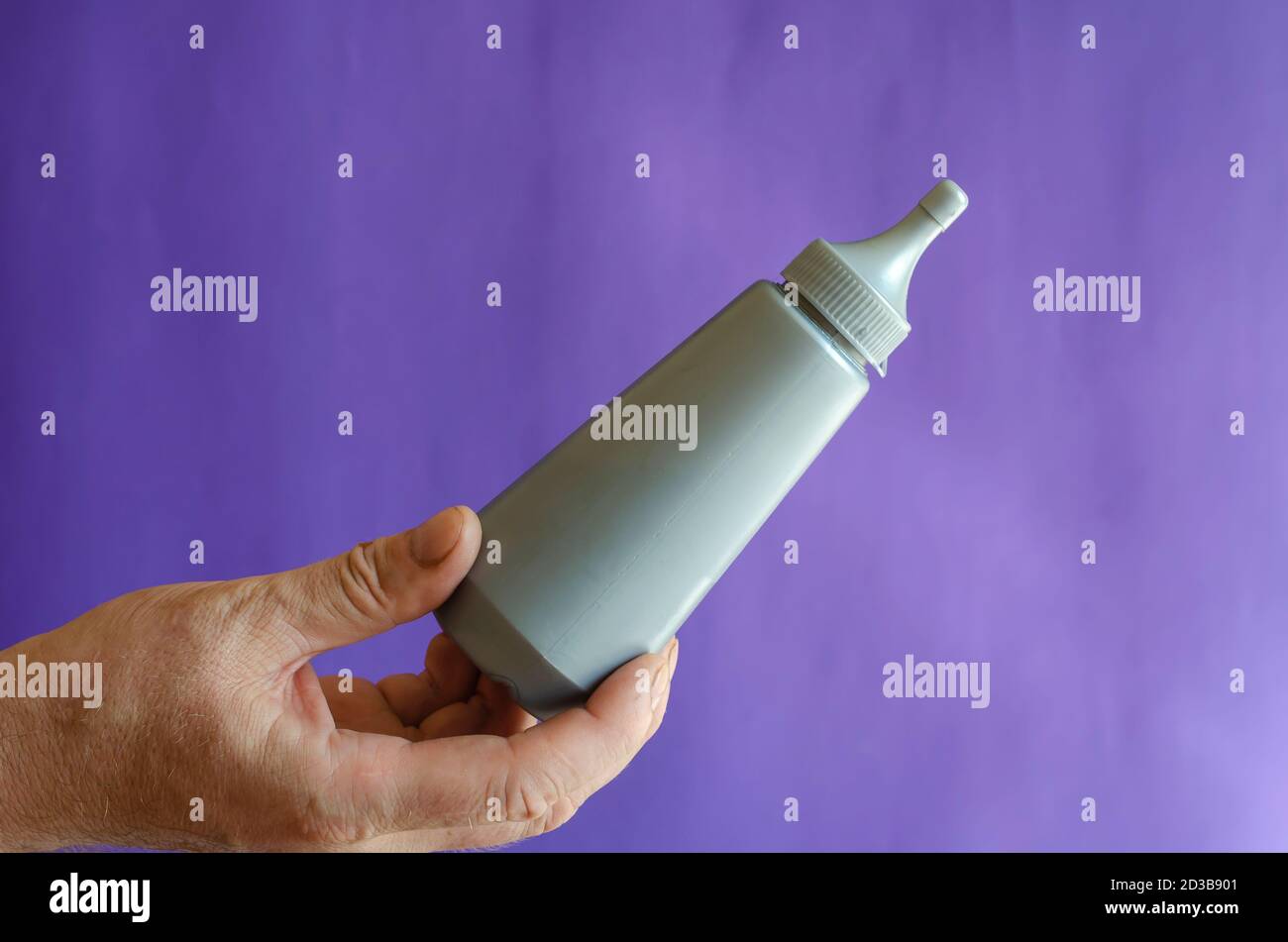 Männliche Hand und graue Plastikflasche mit Sirup. Der Mann hält eine neue Flasche Süßsirup für Eis und Desserts. Selektiver Fokus. Stockfoto