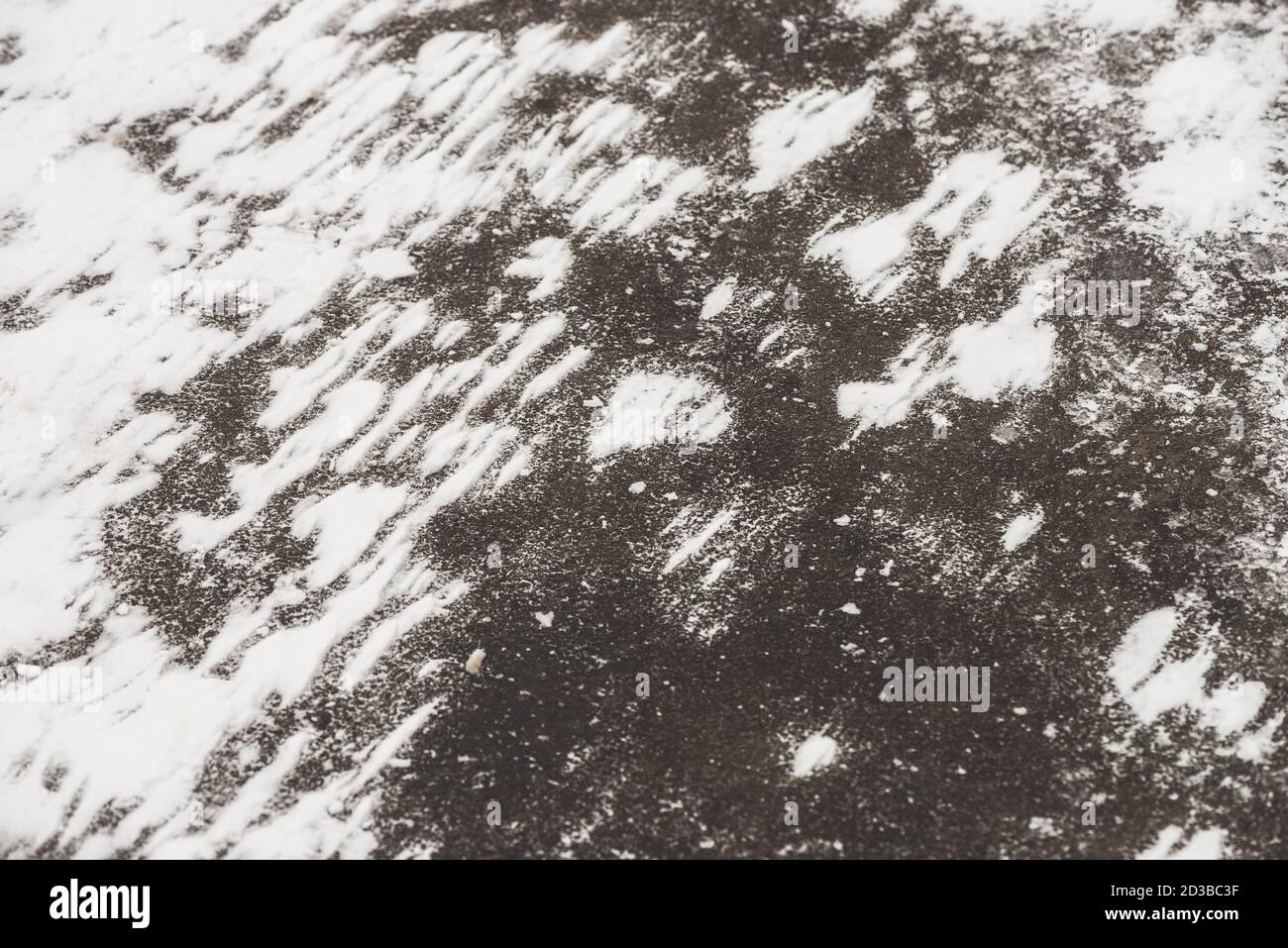 Rutschige Straßen. Verschneite Spur auf Gehweg. Texturierter Winterhintergrund von Asphalt mit verschneiten Drifts aus nächster Nähe. Schneesturm auf der Straße mit Kopierplatz. Zusammenfassung Stockfoto