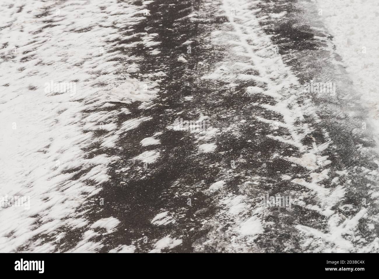 Rutschige Straßen. Spur von Reifenprofil auf Schnee. Texturierter Winterhintergrund von Asphalt mit verschneiten Drifts aus nächster Nähe. Schneesturm auf der Straße mit Kopierplatz. Ab Stockfoto