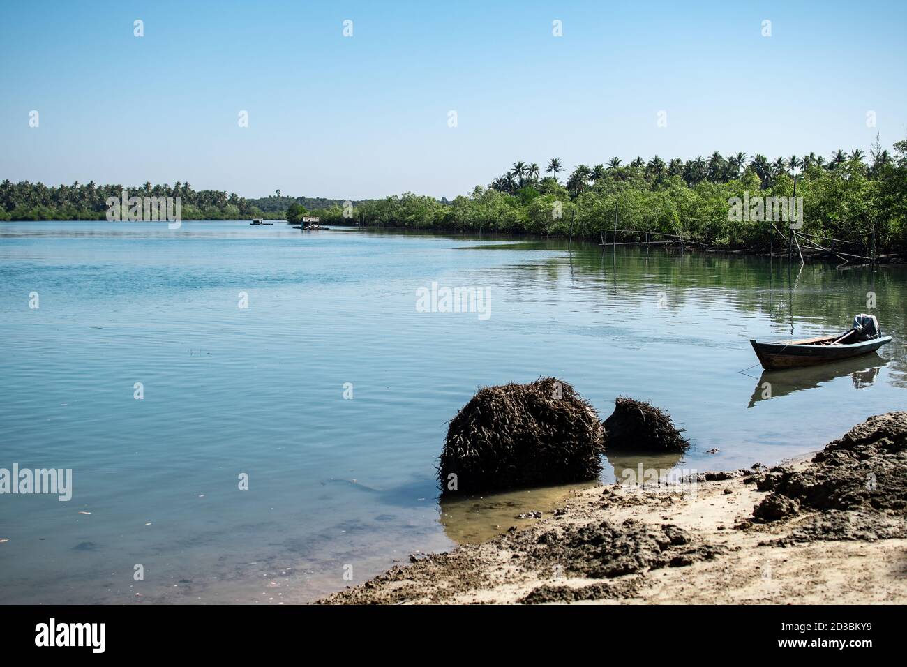 Ein kleines Holzboot in einem türkisfarbenen Fluss mit saftig grünen Mangrovenbäumen, die auf jeder Seite in Ngwesaung, Myanmar wachsen Stockfoto