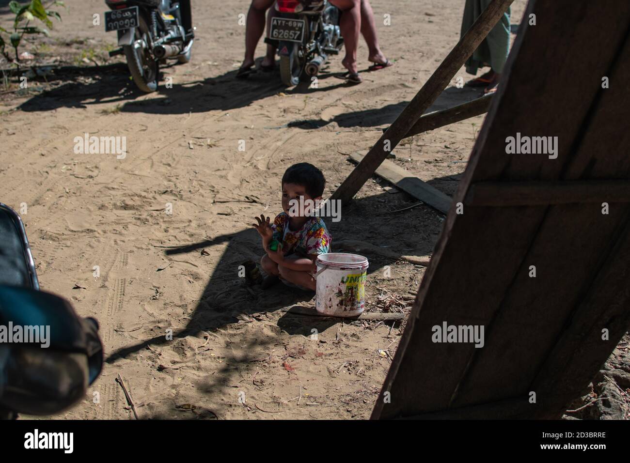 Ngwesaung, Myanmar - 26. Dezember 2019: Ein junges burmesisches Kind in einem bunten Kleid sitzt am 26. Dezember 2019 in Ngwesaung Myanmar im Sand und den Wellen Stockfoto