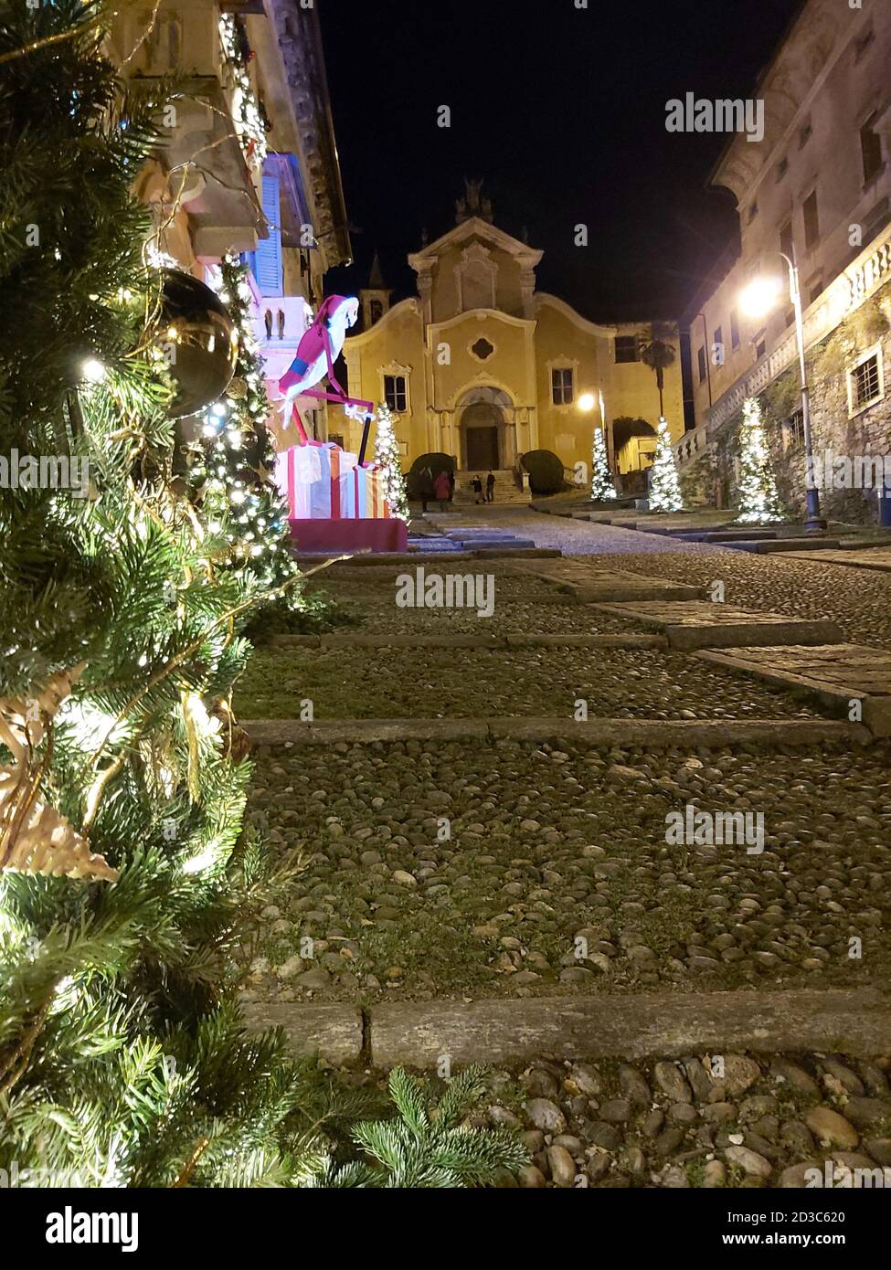 Avenue voll von Weihnachtsbäumen alle beleuchtet, mit Sternen und goldenen Kugeln, am Ende der Straße können Sie eine alte italienische Kirche zu sehen Stockfoto