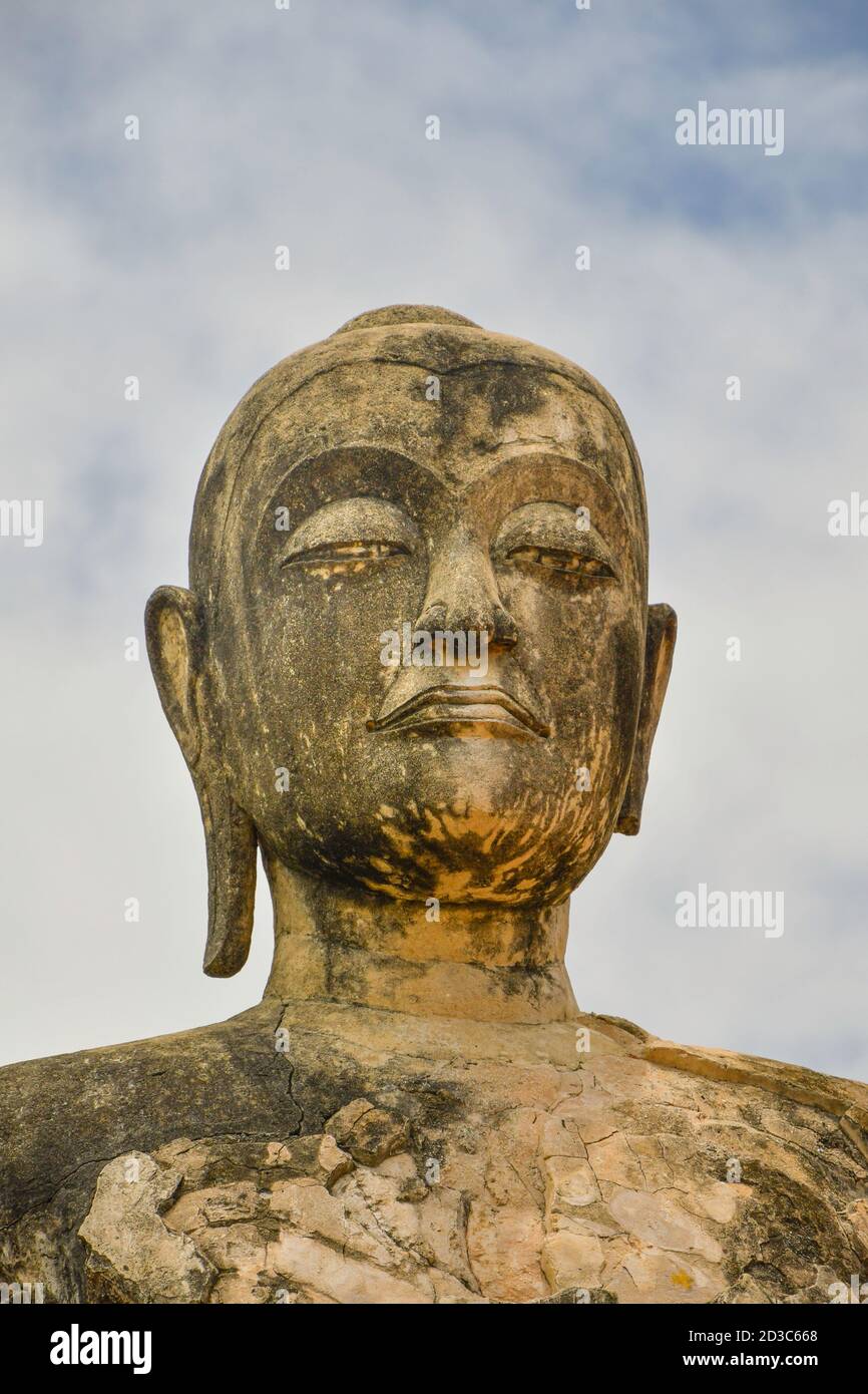 Der steinerne Kopf einer großen buddha-Statue vor einem Himmelshintergrund. Die buddhistische Statue hat einen ihrer länglichen Ohrläppchen verloren. Stockfoto