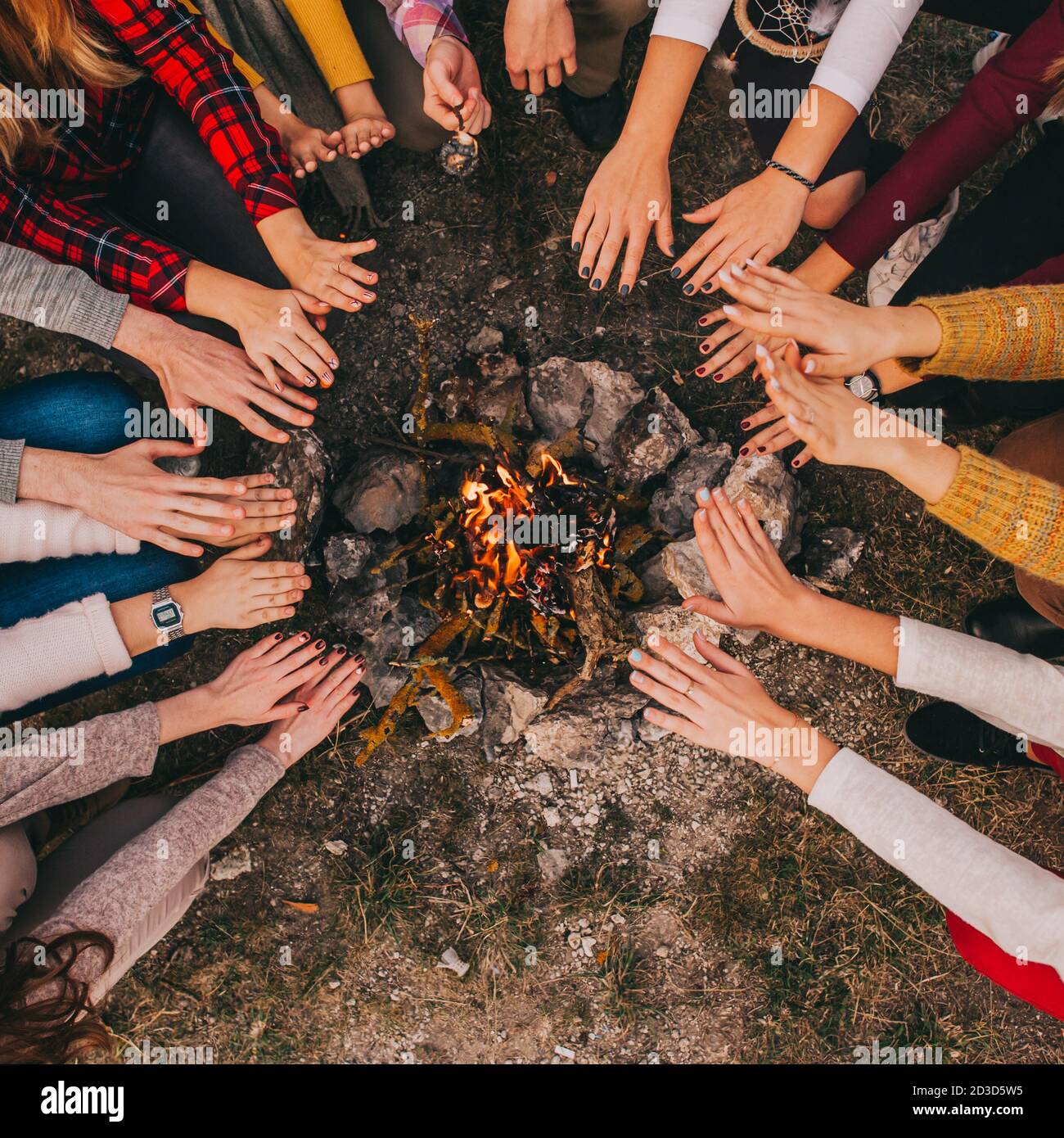 Draufsicht auf junge Camper sitzen herum und wärmen ihre Hände auf einem Lagerfeuer im Herbst. Nahaufnahme der Hände von Freunden Jungen und Mädchen über Feuer. Kontra Stockfoto