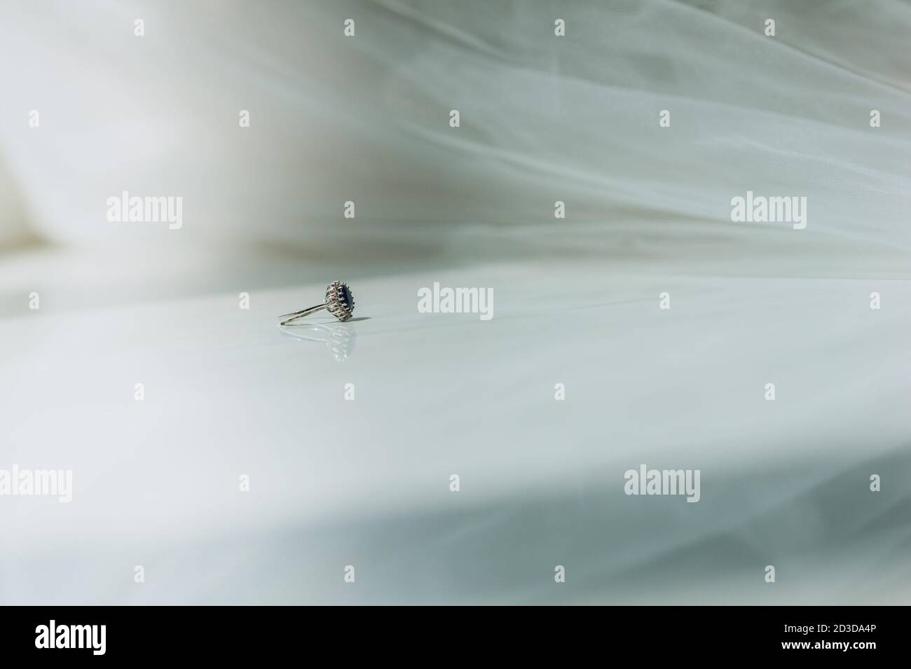 Nahaufnahme eines eleganten exquisiten Vintage-Rings mit einem blauen Diamanten auf der Fensterbank in der Nähe des Schleiers. Morgen der Braut. Hochzeitsdetails. Selektive Stockfoto