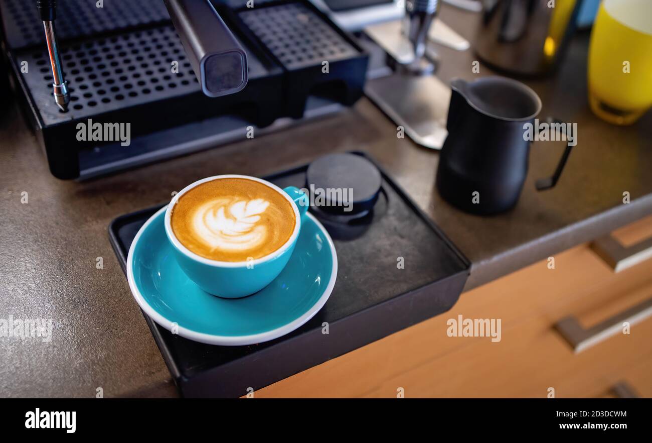 Latte Kaffee Zubereitung von Amateur zu Hause. Eine Tasse frischer Cappuccino, zubereitet zu Hause. Kaffeemaschine und Küche im Hintergrund. Home Barista Stockfoto
