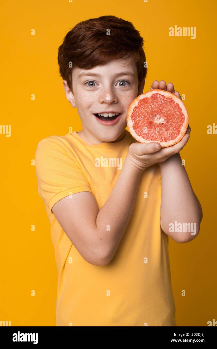 Kaukasischer Ingwer Junge mit Sommersprossen zeigt bei Kamera A Grapefruit gestikuliert Überraschung auf einer gelben Studiowand Stockfoto