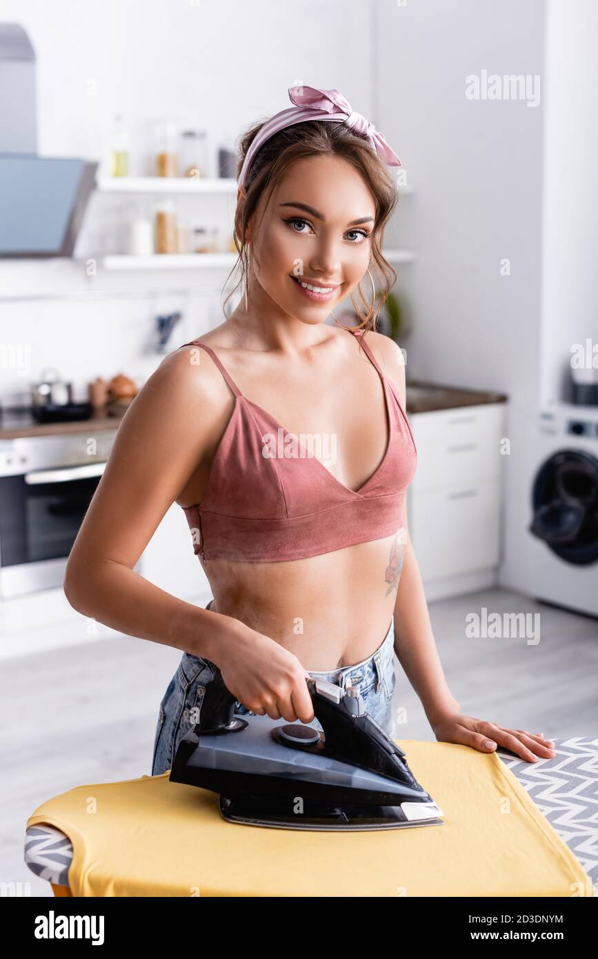 Junge Hausfrau Bügeln T-Shirt und Blick auf Kamera zu Hause Stockfoto