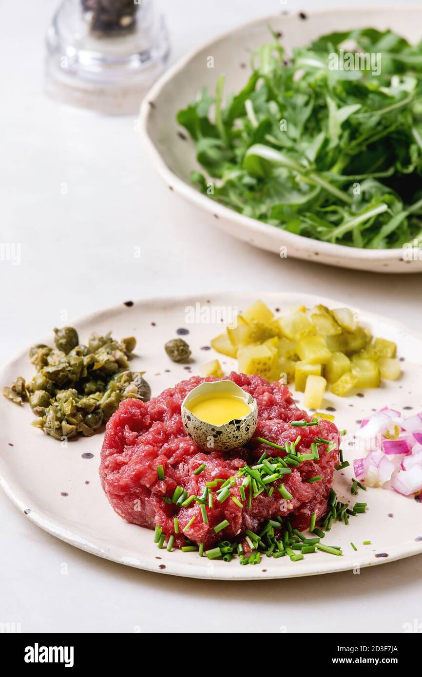 Beef Tartare mit Wachteleier in der Schale, schneiden Gewürzgurken, Kapern, Zwiebeln, Schnittlauch und Rucola Salat in beschmutzt, keramischen Platten mit Pep Stockfoto