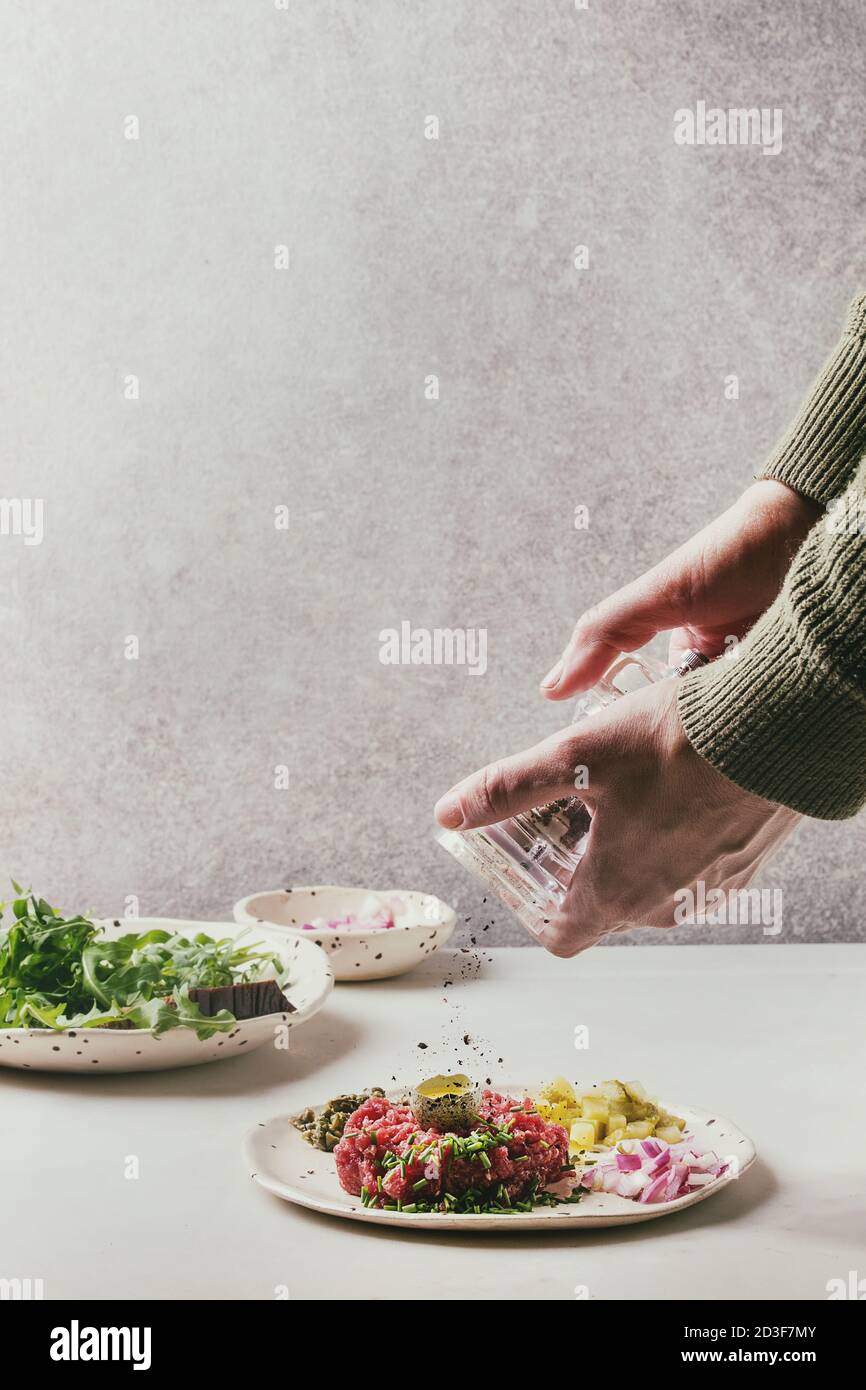 Beef Tartare mit Wachteleier in der Schale, schneiden Gewürzgurken, Kapern, Zwiebeln, Schnittlauch und Rucola Salat in beschmutzt, keramischen Platten auf Weiß Stockfoto