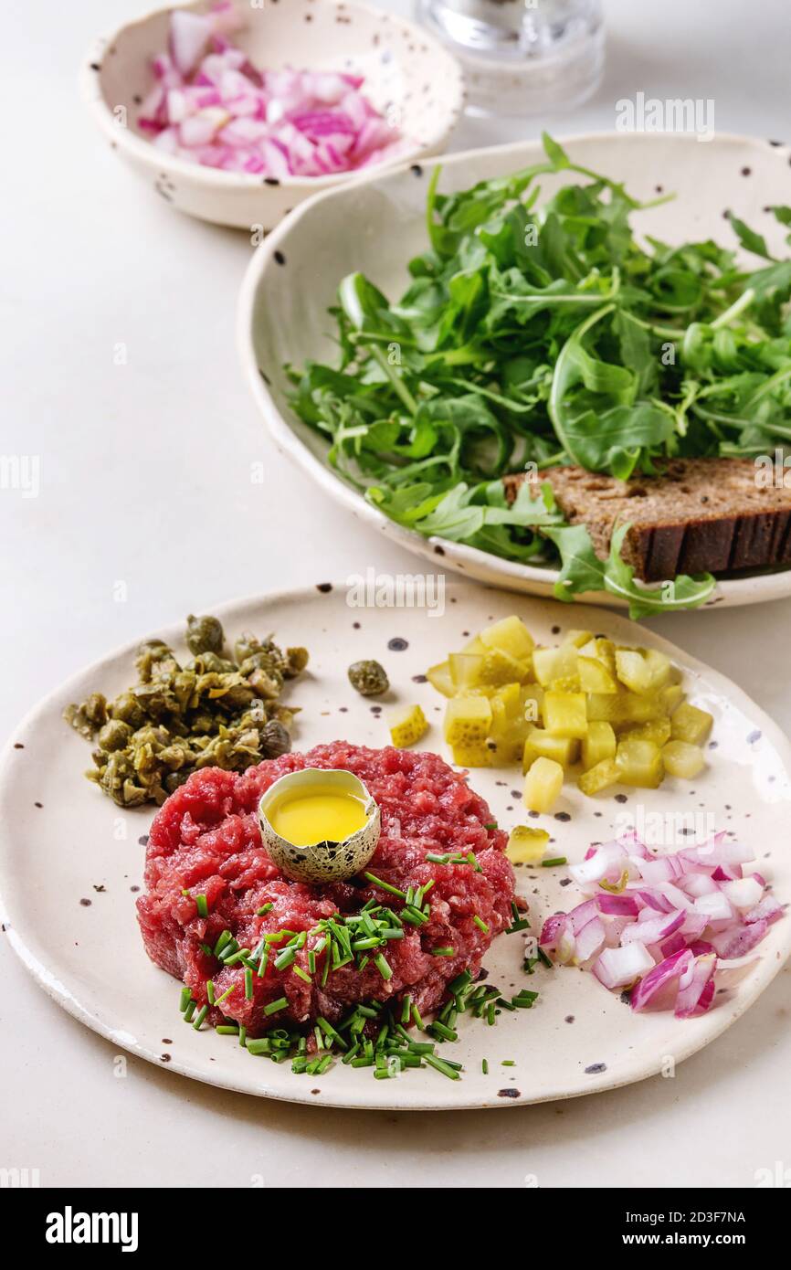 Beef Tartare mit Wachteleier in der Schale, schneiden Gewürzgurken, Kapern, Zwiebeln, Schnittlauch und Rucola Salat in beschmutzt, keramischen Platten mit Pep Stockfoto