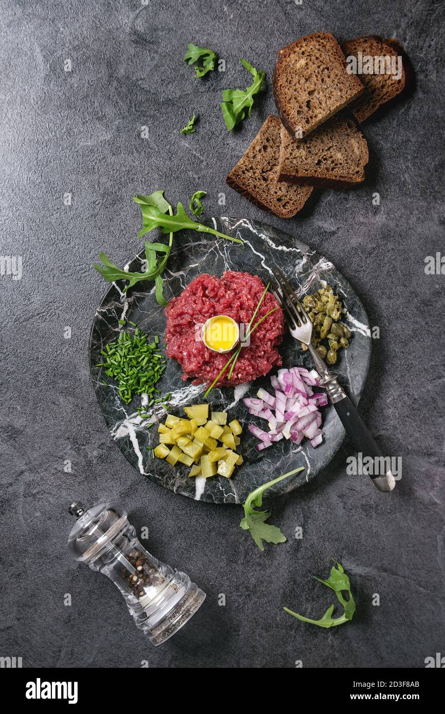 Beef Tartare mit Wachteleier in der Schale, schneiden Gewürzgurken, Kapern, rote Zwiebel, Schnittlauch, Brot, Rucola Salat in Marmor Platten mit Pfeffer m serviert. Stockfoto