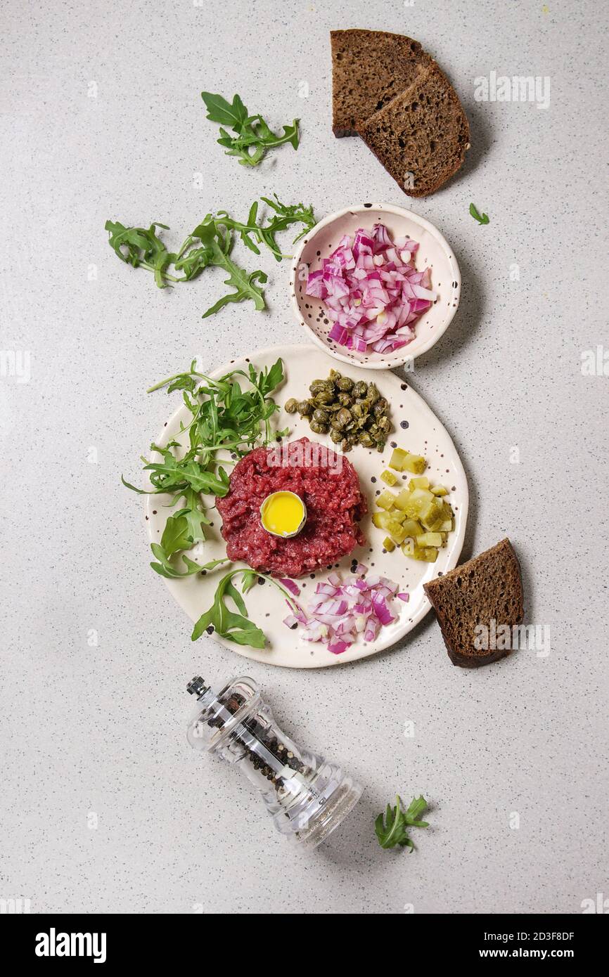 Beef Tartare mit Wachtelei, in der Schale, Brot, schneiden Gewürzgurken, Kapern, roten Zwiebeln, Rucola Salat in beschmutzt, keramischen Platten mit Pfeffer Stockfoto