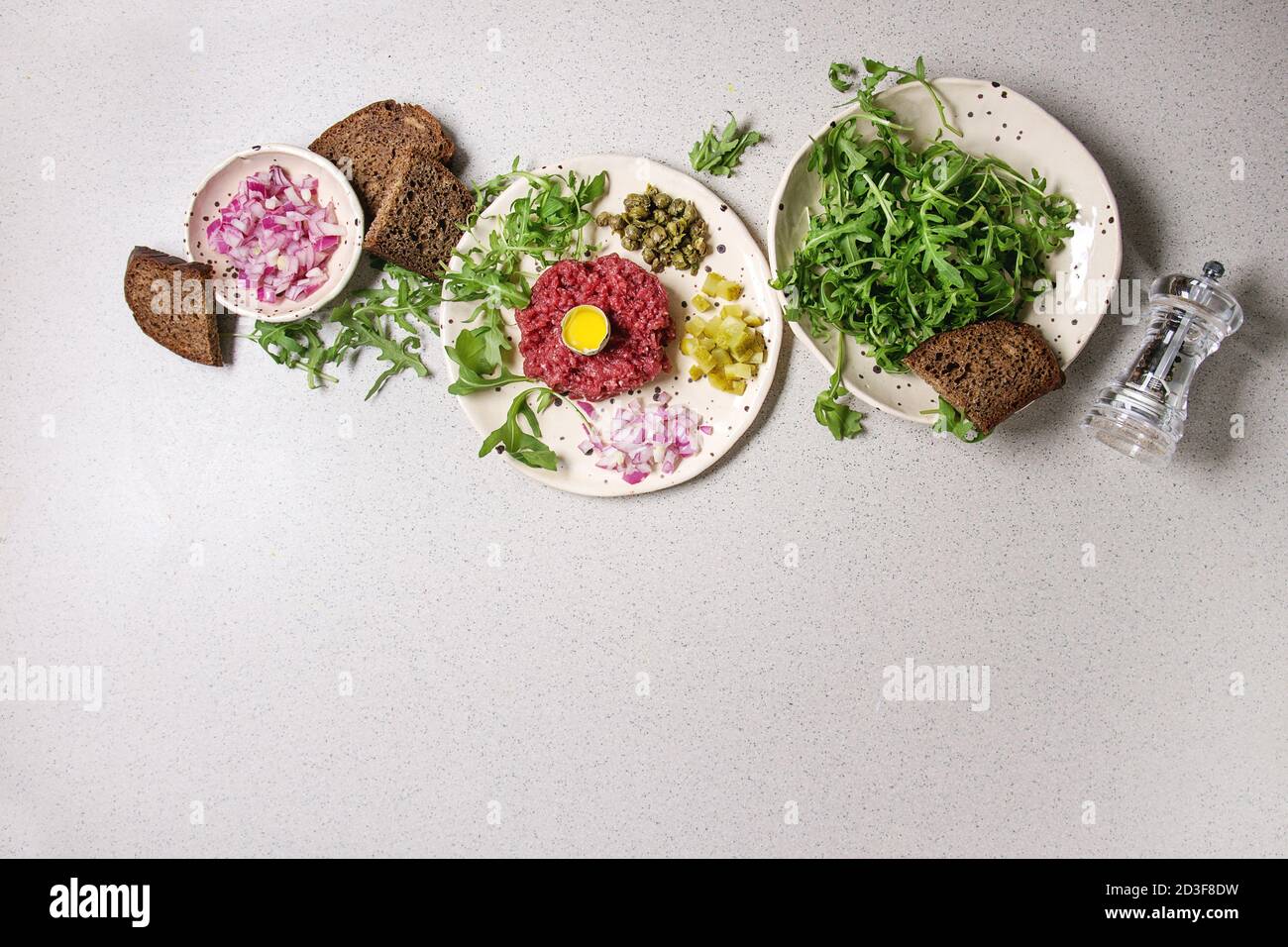 Beef Tartare mit Wachtelei, in der Schale, Brot, schneiden Gewürzgurken, Kapern, roten Zwiebeln, Rucola Salat in beschmutzt, keramischen Platten mit Pfeffer Stockfoto