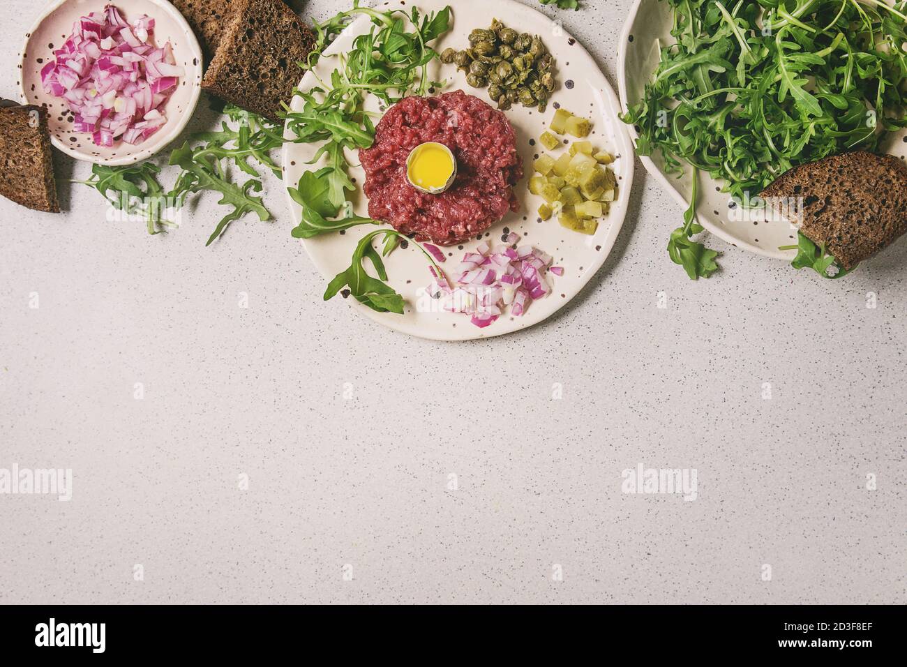 Beef Tartare mit Wachtelei, in der Schale, Brot, schneiden Gewürzgurken, Kapern, roten Zwiebeln, Rucola Salat in beschmutzt, keramischen Platten mit Pfeffer Stockfoto