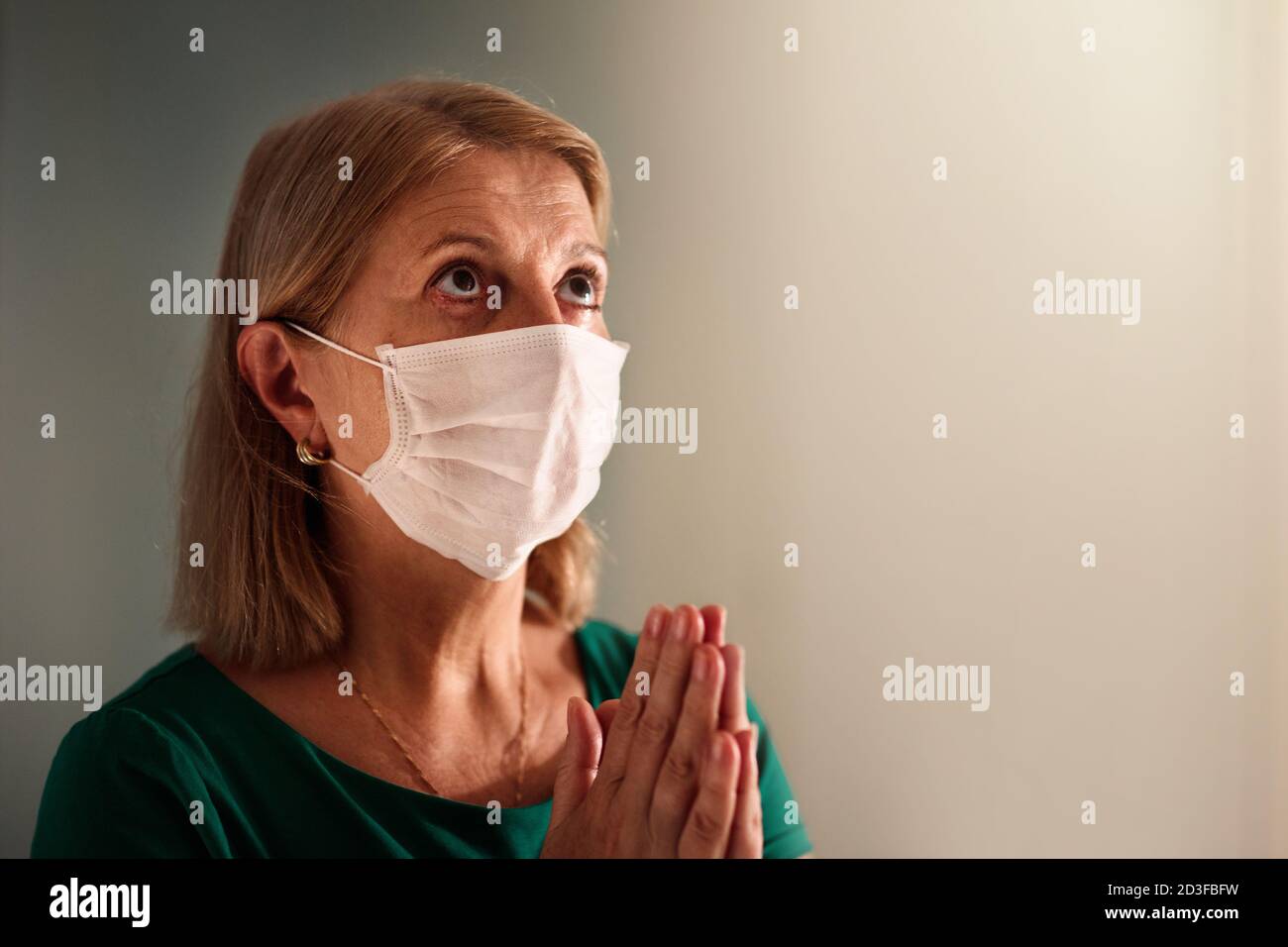 Betet für das Opfer des Coronavirus. Frau in Gesichtsmaske beten für krank. Seniorpatient in Krankenhauskapelle oder Kirche während des Covid-19-Ausbruchs. Viruspandemie Stockfoto