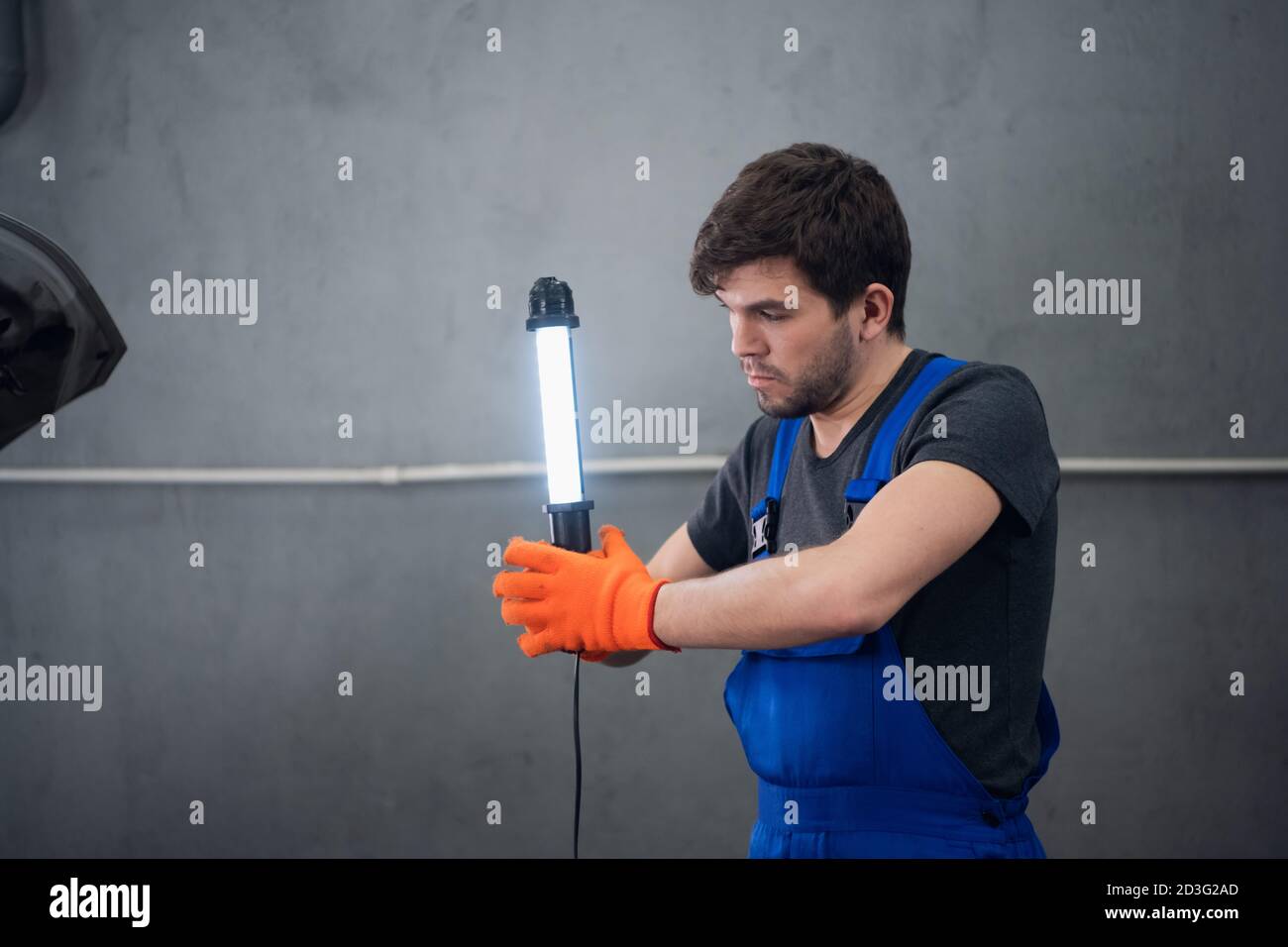 Ein Mann in Overalls und Arbeitshandschuhen hält eine Taschenlampe Stockfoto