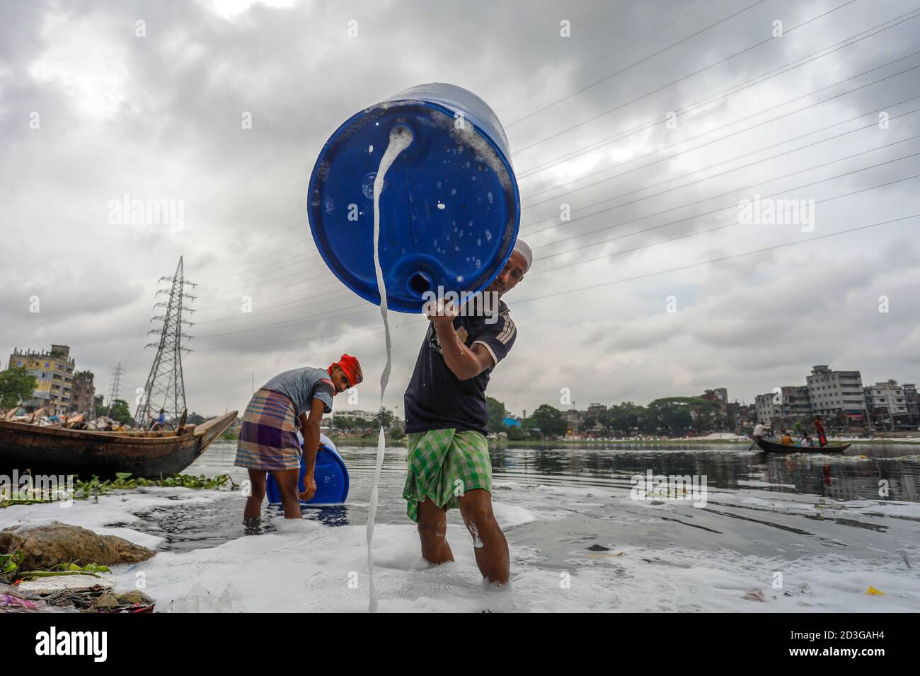 Männer aus Bangladesch waschen leere Plastikfässer, die zum Transport von Chemikalien verwendet wurden, im Wasser des Buriganga-Flusses, bevor sie sie recyceln, in Dhaka, Bangl Stockfoto